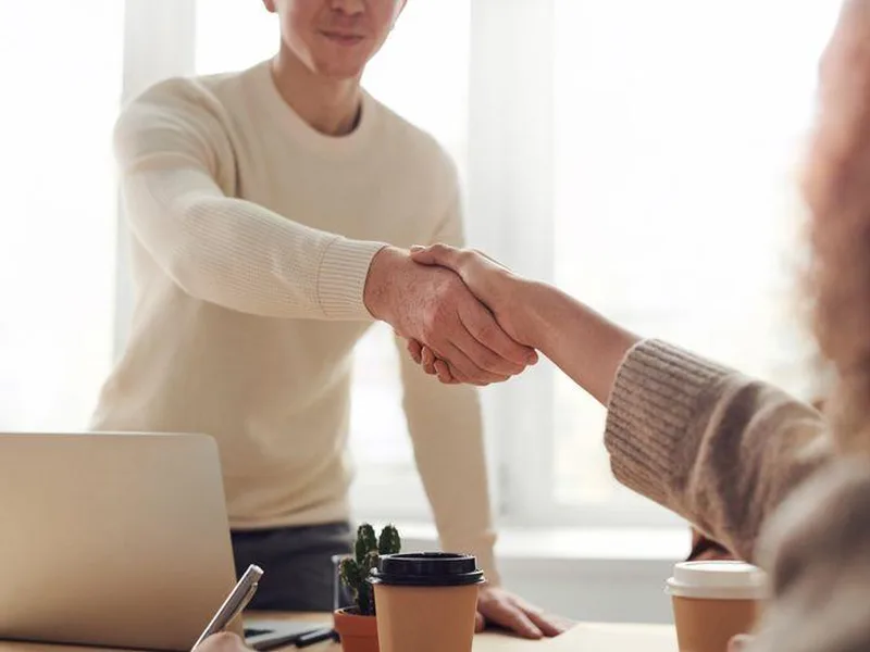 Two people shaking hands across a desk in a bright office